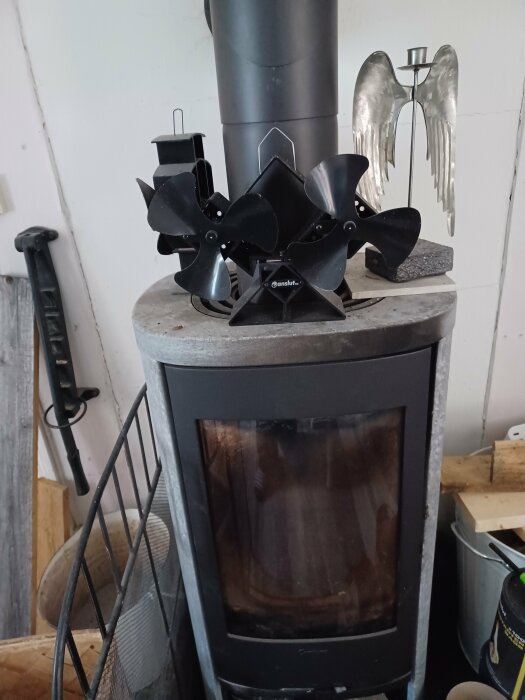 Vardagsrumskamin med två svarta kaminfläktar ovanpå, en dubbel och en enkel, bredvid en ängelljusstake i metall.