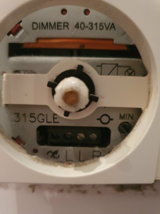 Närbild på en trasig dimmer med texten "DIMMER 40-315VA" och "315GLE", placerad i ett badrum, använd för att styra glödlampor.