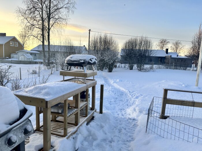 Snötäckt bakgård med pizzaugn och grillbord i vinterlandskap.