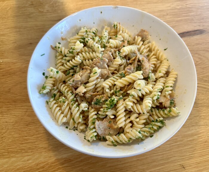 En tallrik med krämig pasta med kyckling och örter på ett träbord.