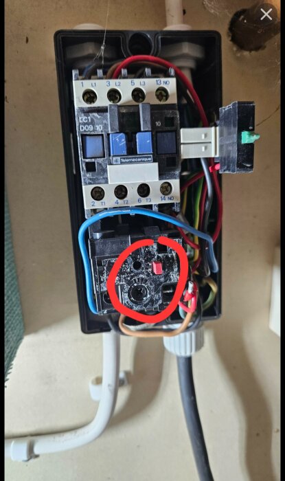 Bild av en elektrisk kopplingsbox med flera anslutna kablar och omkopplare, markerad med en röd cirkel runt en komponent.