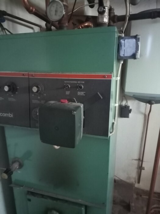 Grön värmepanna med rör och mätare, placerad i en industriell miljö.