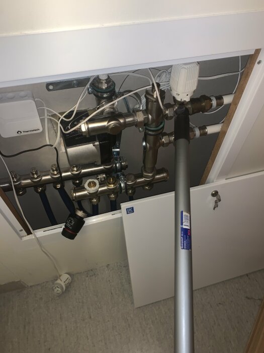 Bild av ett värmesystem med rör och ventiler, där en pinne pekar mot ett vitt värmereglage.