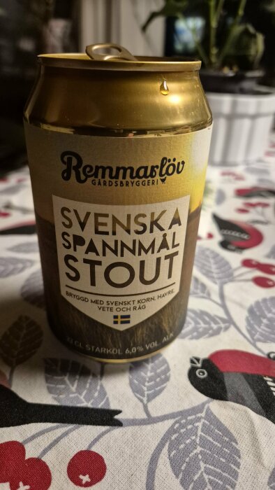 En burk Remmarlöv gårdsbryggeri svensk spannmål stout med fokus på etiketten, på ett mönstrat bord.