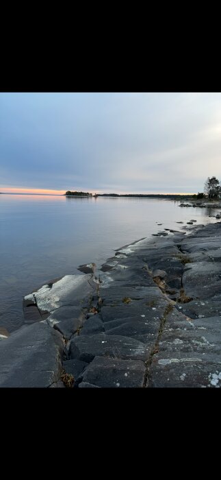 Sjölandskap vid Vänern med klippor i förgrunden och horisont vid solnedgång.