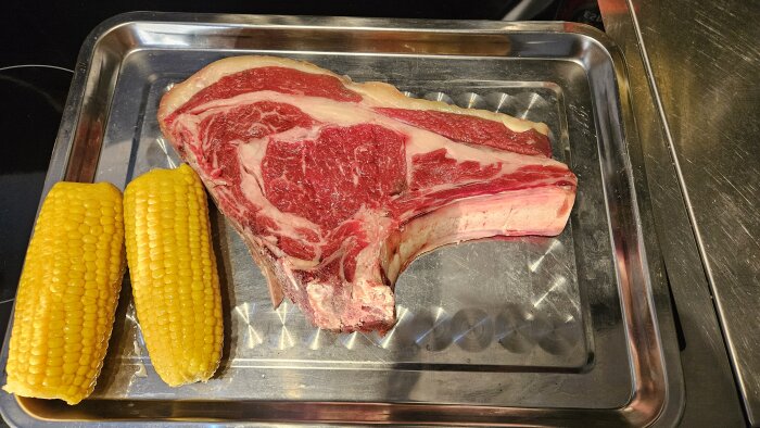 Grillad Lomo Alto-köttskiva med ben och kappa på en bricka, serverad med två majskolvar.
