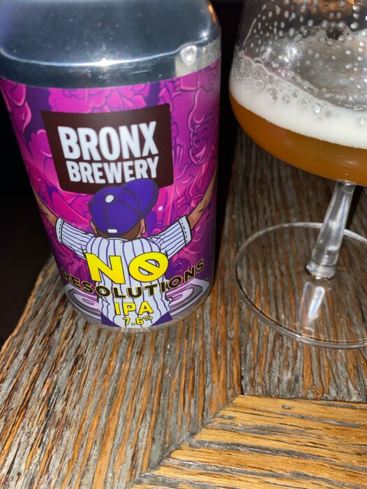 Ölburk med etiketten "No Resolutions IPA 7.6%" från Bronx Brewery bredvid ett glas öl på ett träbord.