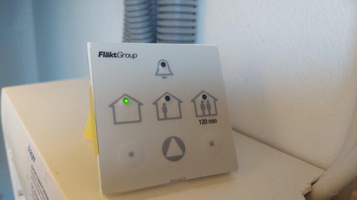Kontrollpanel för FläktGroup-ventilation med en grön lampa som lyser bredvid husikonen, omgiven av andra symboler och texten "120 min".