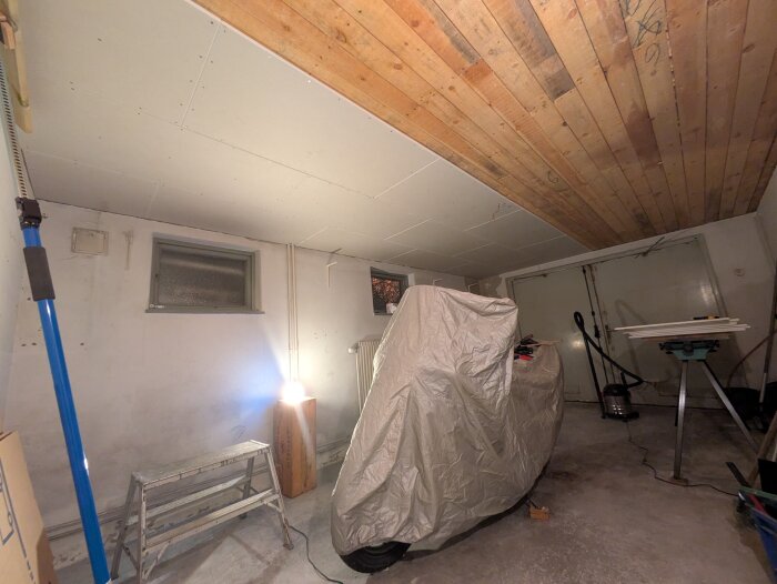 Garage under renovation with covered items, wooden ceiling, and a step ladder in view.