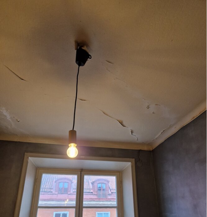 Slitet innertak i behov av renovering, med spackel och färg. Gamla bultar kvar och sprickor syns, glödlampa hänger i mitten av bilden.