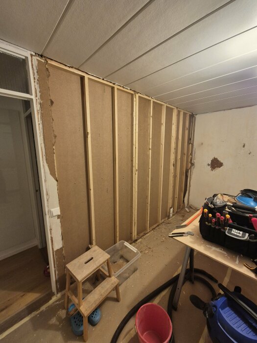 Renovering av ett rum där träfiberskivorna har tagits bort från innerväggen, verktyg och material syns på golvet och bordet i förgrunden.