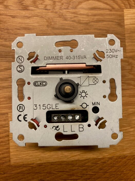 Baksidan av en ELKO dimmer 40-315VA på träyta, visar anslutningar och märkningar som 230V~ 50Hz, använd för halogenlampor.