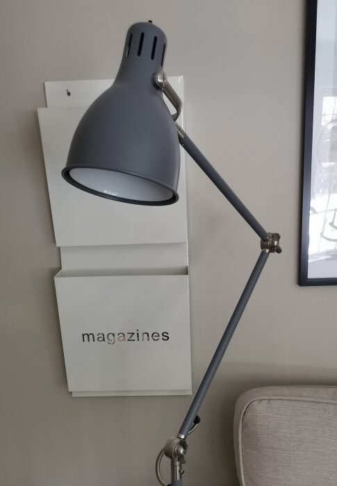 Metallisk golvlampa med justerbar arm framför en vägg med en tidskriftshållare märkt "magazines".