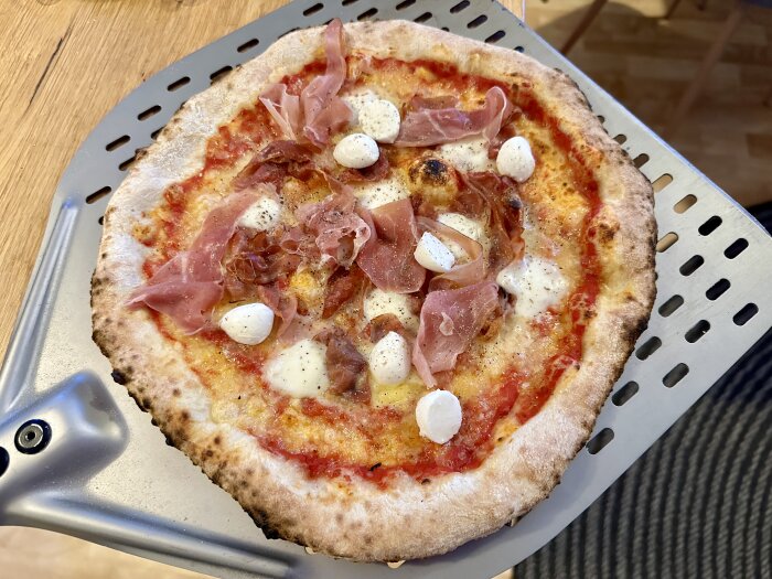 Hemlagad pizza med mozzarella och prosciutto på en bakplåt.