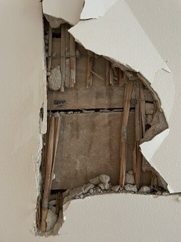 Interior wall with exposed layers: wooden core, straw layer, and plaster/cement. The wall shows a section removed, revealing construction details.