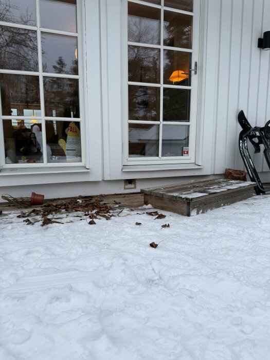 Hål i fasaden under altandörren, omgivet av snö och fallna löv. Ventilationskåpa borttagen, potentiellt frånluft från centraldammsugare.