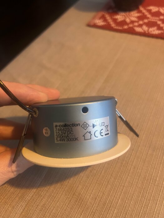 En hand håller en A-collection downlight med specifikationer som 15.5V DC, 5.4W, 3000K, visas på sidan.