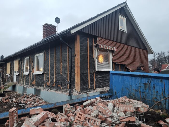 Husrenovering pågår med nedriven fasad, synliga reglar och byggavfall i form av tegel, samt en julstjärna i ett fönster.