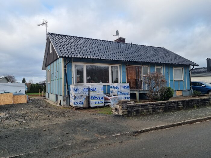 Ett hus under renovering med ny fasadisolering påbörjad, blå presenningar och byggmaterial framför ingången.