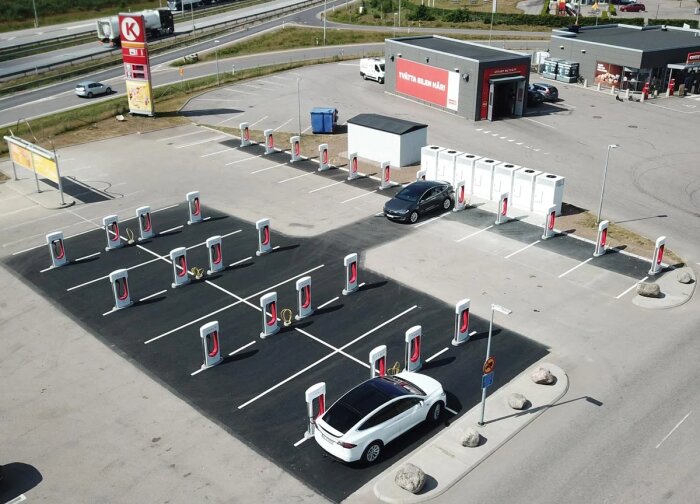 Laddstation vid en bensinmack med flera laddstolpar och två bilar, varav en Tesla, parkerade.