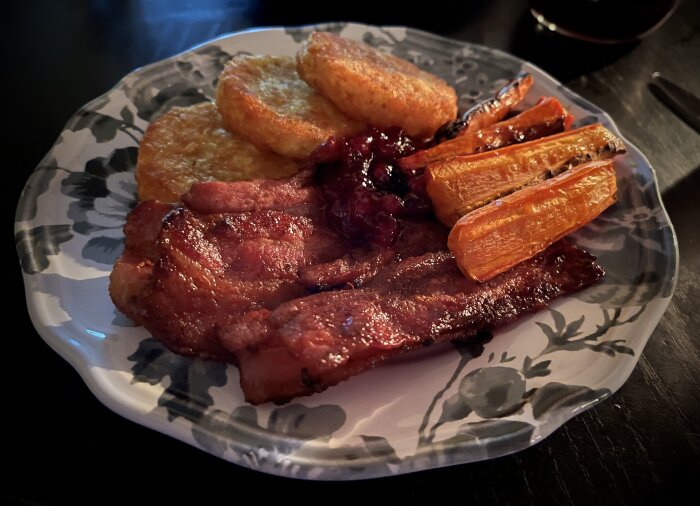 Tallrik med potatisbullar, stekfläsk, ugnstekta morötter och lingonsylt.