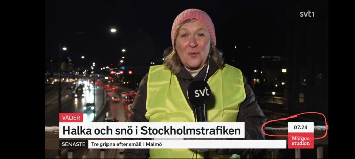 En reporter i gul reflexväst rapporterar om halka och snö i Stockholmstrafiken på kvällen med bilköer i bakgrunden.