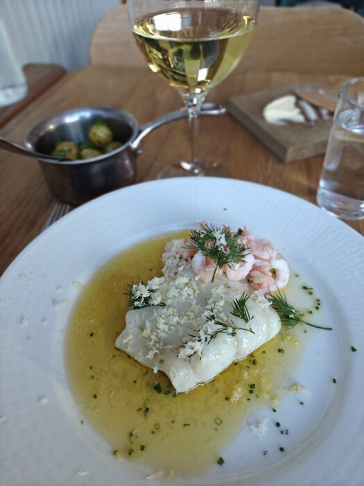 Tallrik med fisk, räkor och dill i smörsås samt ett glas vitt vin i restaurangen Portal.