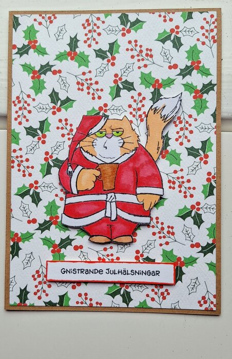 En tecknad katt i tomtedräkt på ett julkort med texten "Gnistrande julhälsningar". Bakgrunden är dekorerad med juliga mönster av gröna blad och röda bär.