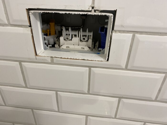 Insidan av en toalettvägg med synlig cistern och flottörmekanism, omgiven av vita kakelplattor.