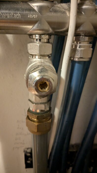 Stängningsventil för en vattenpump, monterad på ett rör med märkning och angränsande kablar, med syfte att identifiera avstängningsventiler.