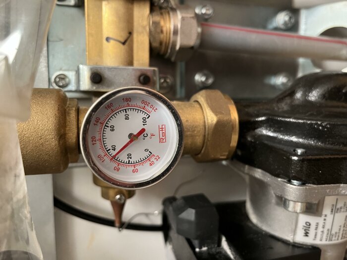 Termometer i fördelarskåpet visar vattentemperatur på ca 50°C i värmesystemet, med rördragning och ventil vid anslutning.