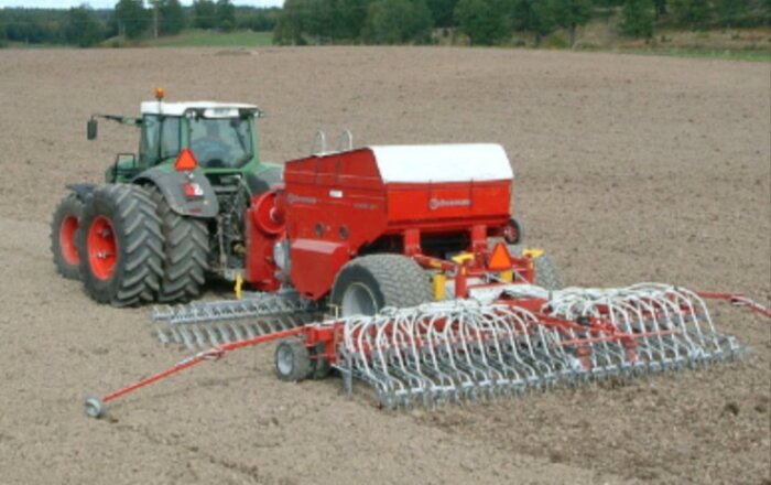 Traktor med såmaskin arbetar på ett fält för att plantera grödor under sässesongen.