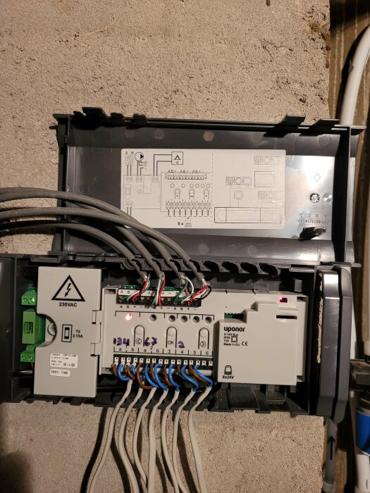 Elcentral med Uponor X-145 styrning, inkopplade kablar för termostater och styrdon visas, detaljerad kopplingsschema på insidan av locket.