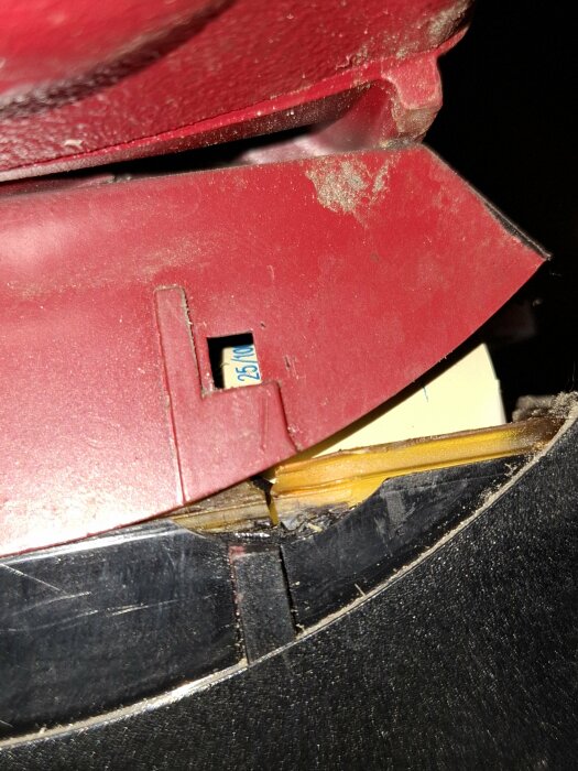 Närbild av en öppnad röd plastkåpa som avslöjar insidan med en synlig kondensator, delvis täckt av smuts och damm.