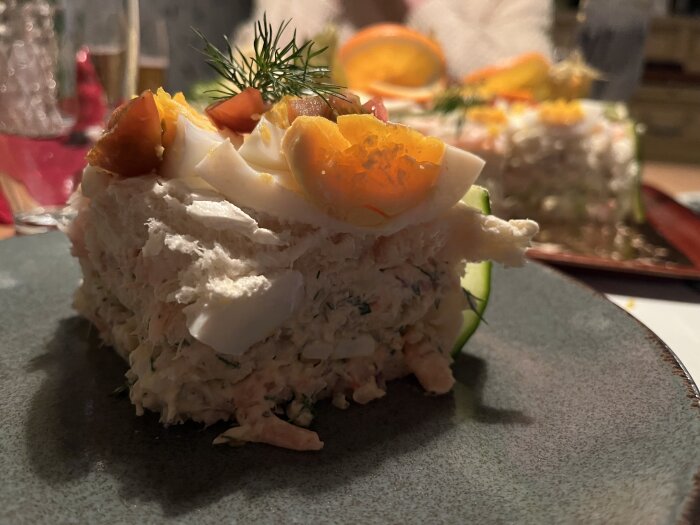 En bit smörgåstårta med dekorationer av ägg, physalis och dill på en tallrik.