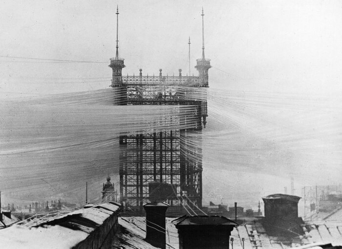 Svartvitt foto av Telefontornet i Stockholm omkring 1890, med ett nätverk av telefonlinjer som sträcker sig ut från tornet över stadens tak.