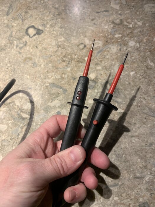 Multimeterprober i en hand på stengolv.