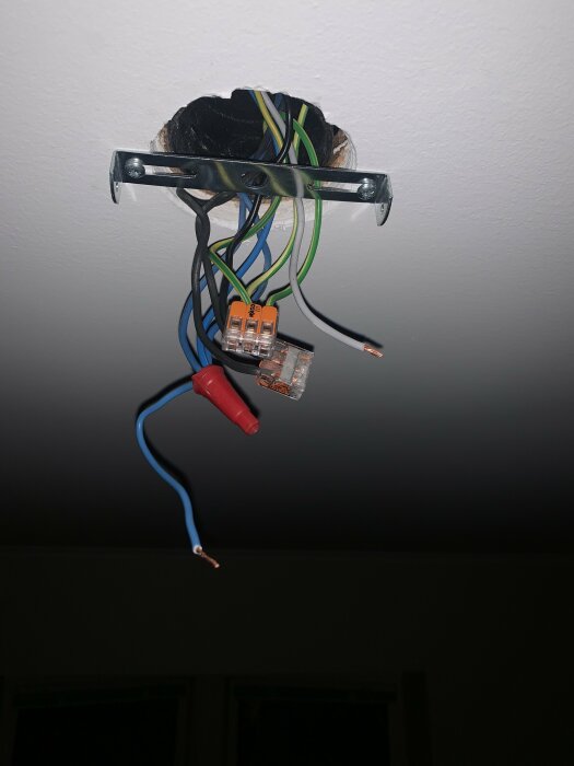 Elektriska kablar och kopplingsplintar hänger från ett tak, med ett metallfäste synligt runt kablarna.