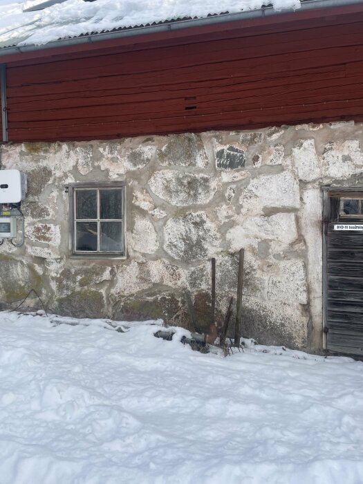 Fasad av en ladugård med blandad puts, fönster och snötäcke i förgrunden, planerad renovering med cementputs.