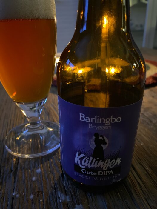 Mörk ölflaska från Barlingbo Bryggeri med etiketten "Källingen Gute DIPA" bredvid ett fyllt ölglas på ett träbord.