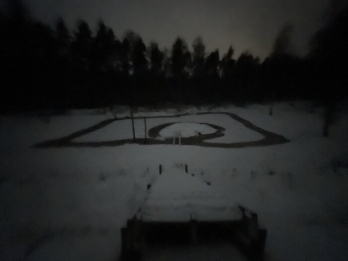 Snötäckt landskap i mörker med begränsad sikt, en slingrande stig i mitten omgiven av träd och himmel.