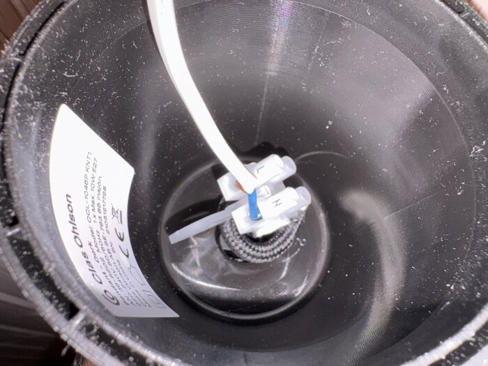 Plastcylinder med lamputtag och kablar anslutna via en sockerbit; etikett med produktinformation från Clas Ohlson synlig inuti.