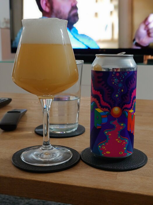 Ett glas öl från Omnipollo bredvid en PIM-ölburk med färgglad design på ett bord.