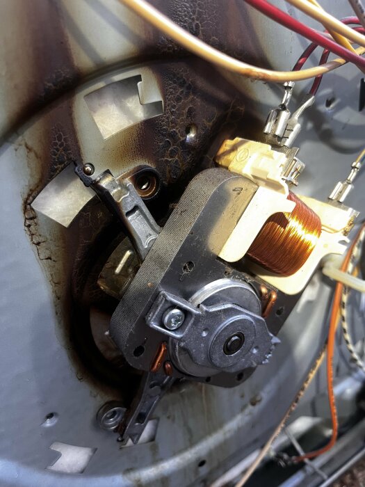 Brännmärken runt fläktmotor i en Siemens inbyggnadsugn, sladdar synliga.