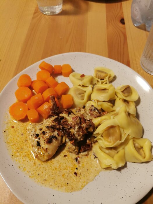 Kycklinglårfilé i sås med vitlök, soltorkade tomater och chili, serverad med pastakuddar arrabbiata och morotsbitar på vit tallrik.