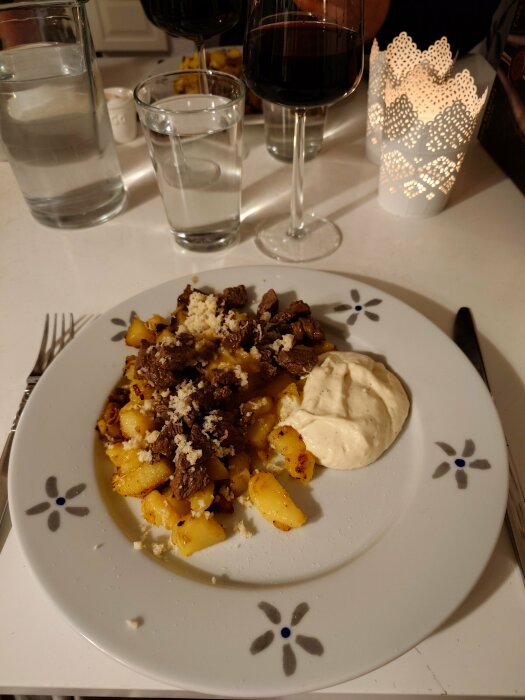 Tallrik med Biff Rydberg, potatis och senapskräm på ett bord med glas, karaff och ljuslykta i bakgrunden.
