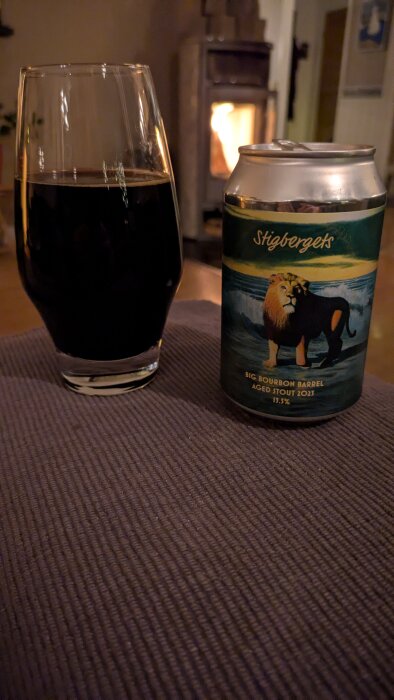 Ett glas mörk stout och en burk med etiketten "Stigbergets Big Bourbon Barrel Aged Stout 2023" framför en kamin.