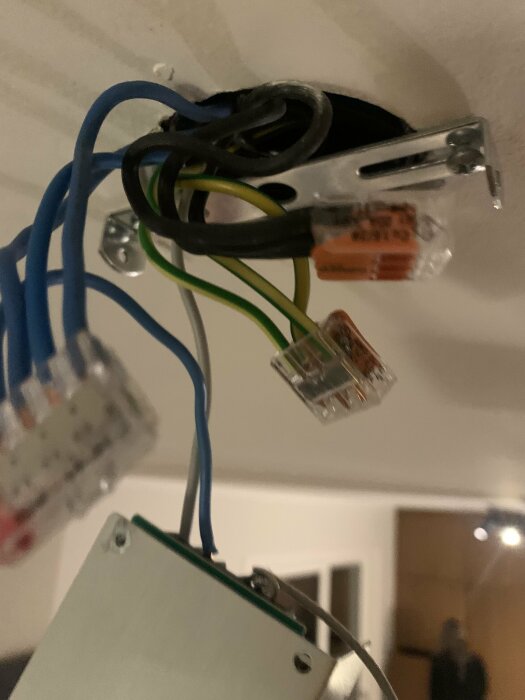 Elektrisk kopplingsanordning med gröngula jordtrådar i Wago-kontakter, visar takfäste för lampa.