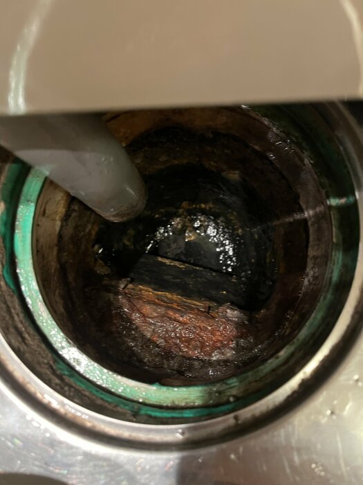 Gjutjärnsbrunn i badrum med tydlig korrosion och slitage, möjlig källa till svag avloppslukt.