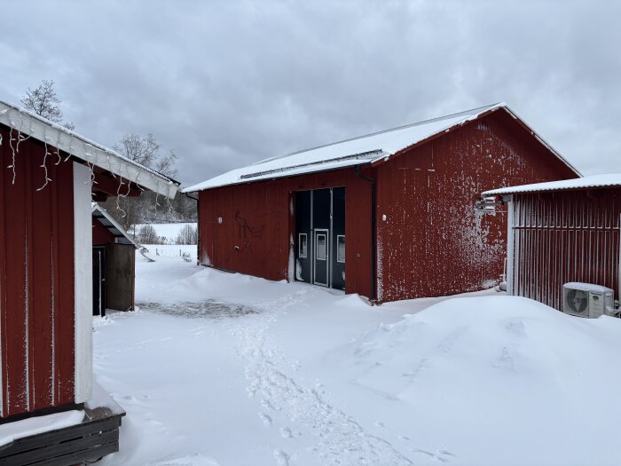 Rött garage med snötäckta tak och omgivningar, redo för användning som verkstad.